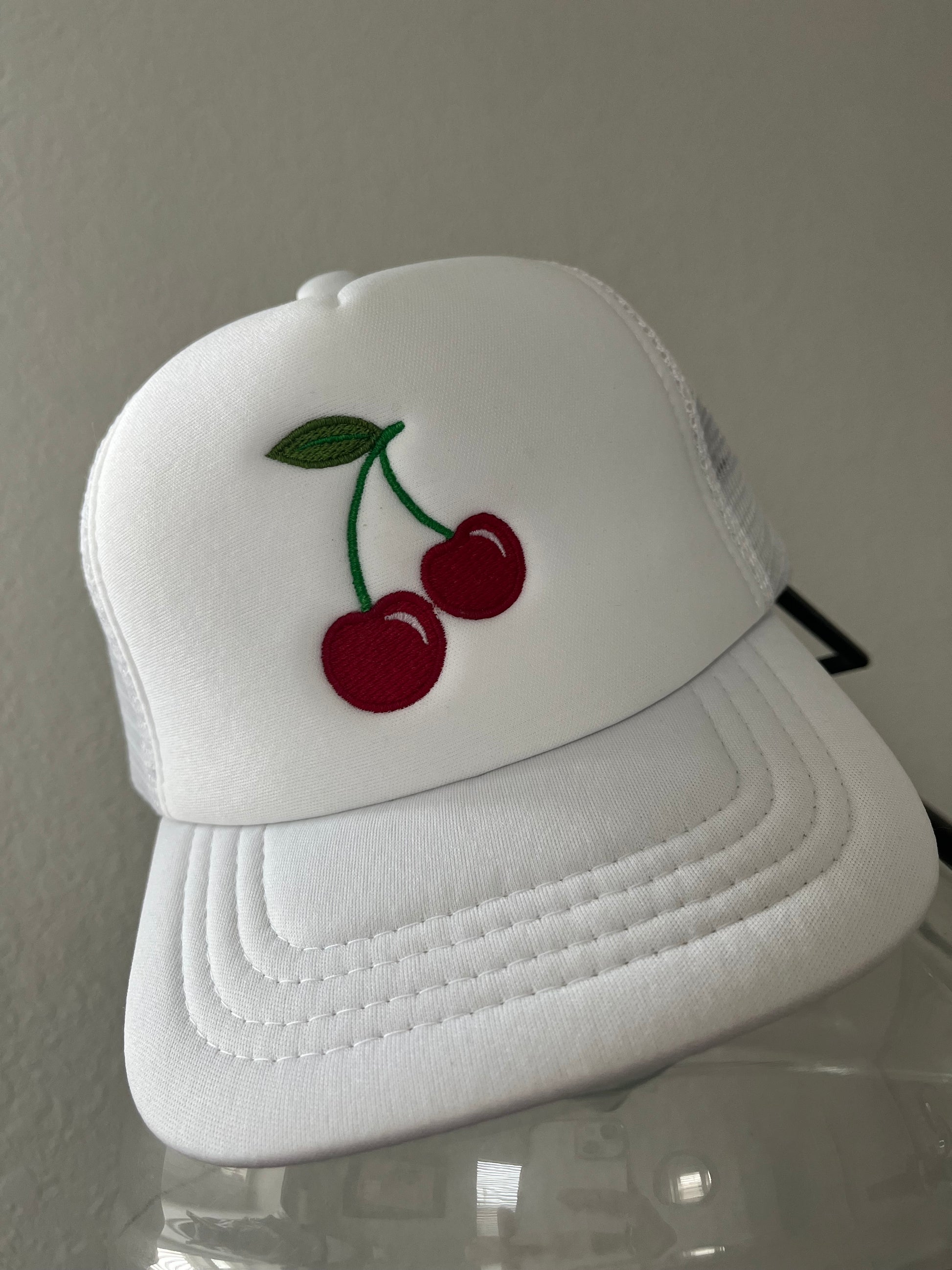 White baby trucker hat with red cherries on a light gray background