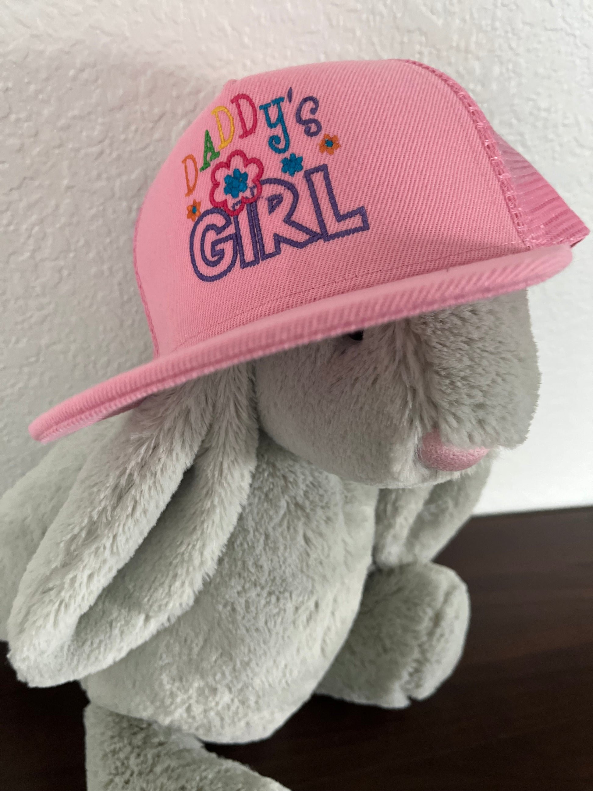 Gray plush toy wearing a pink cap with 'Girl's Girl' text on a white background