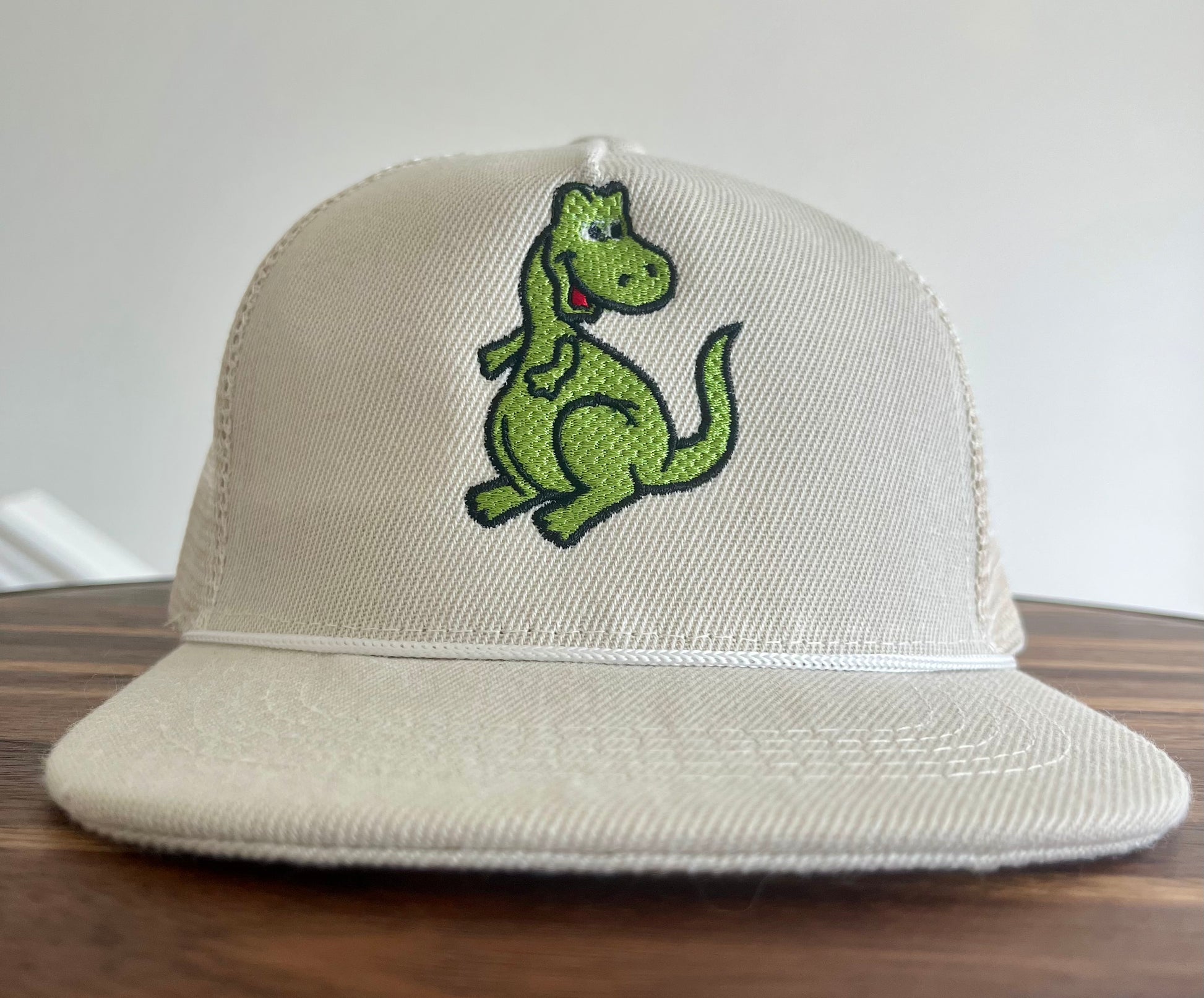 Beige cap with a green dinosaur design on a wooden surface