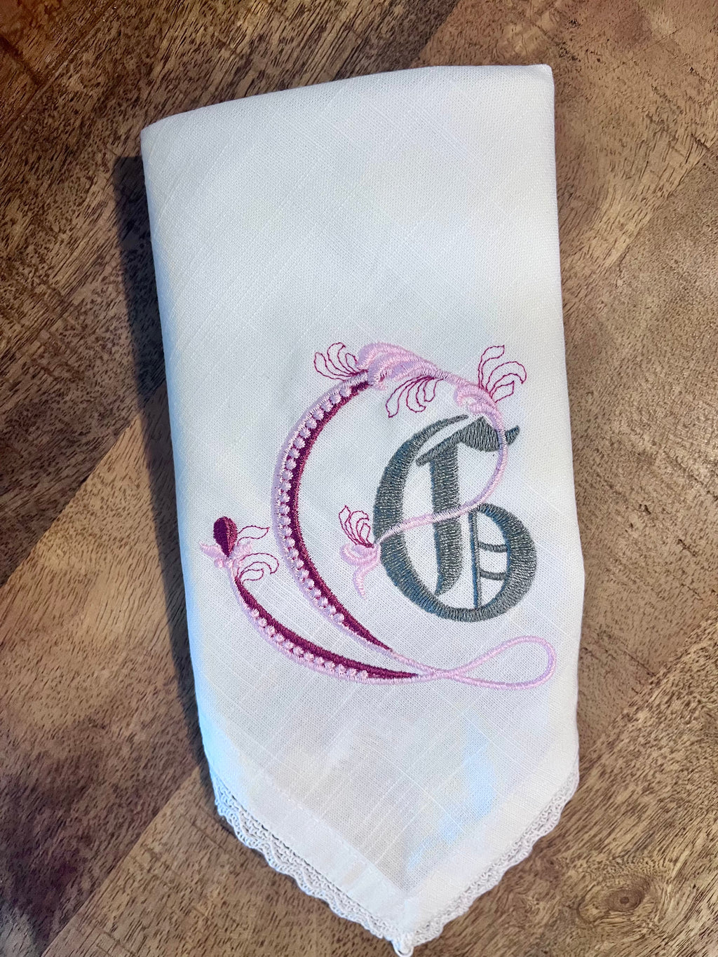 Embroidered cloth napkin with a decorative letter 'G' on a wooden surface