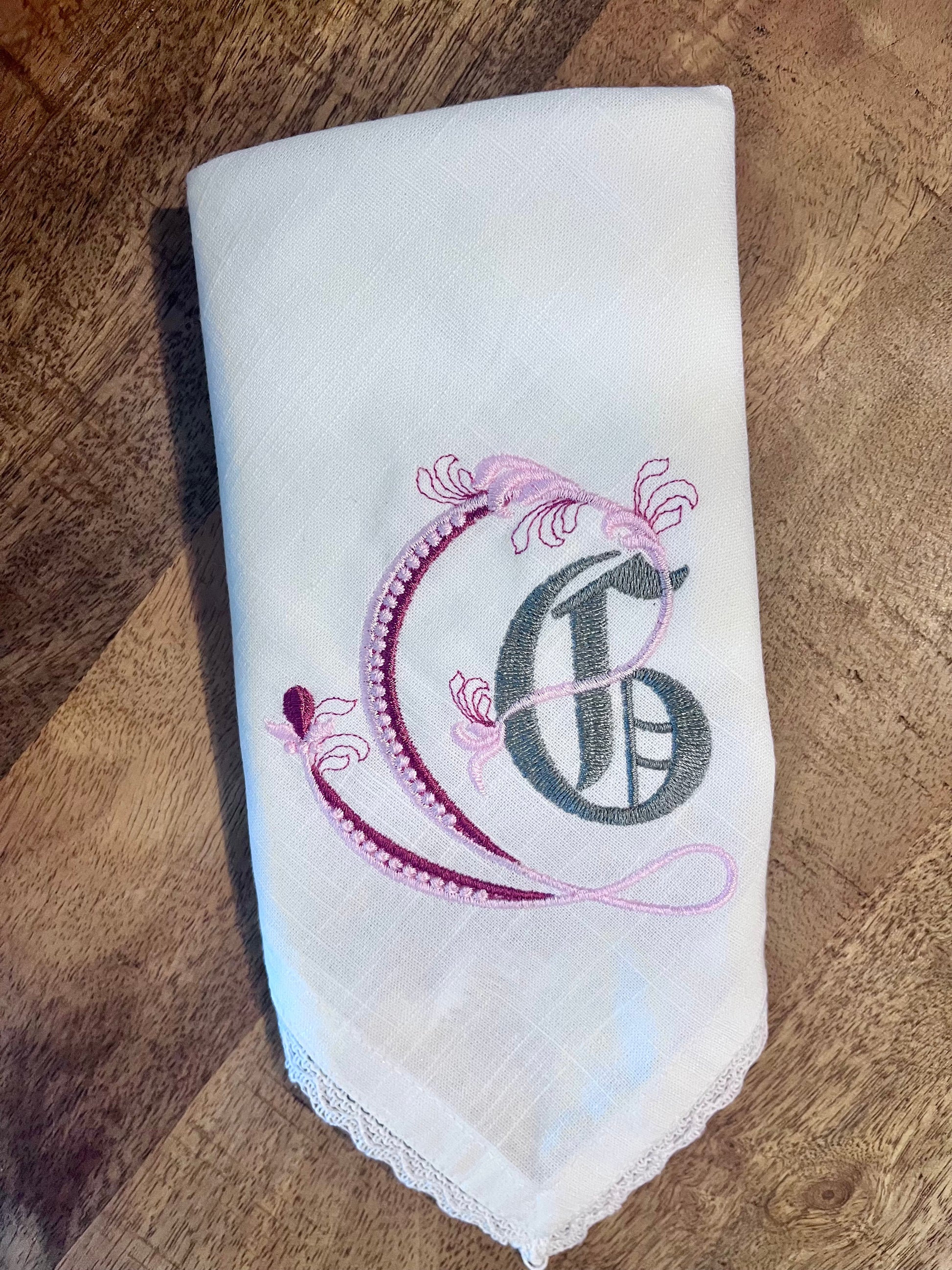 Embroidered cloth napkin with a decorative letter 'G' on a wooden surface