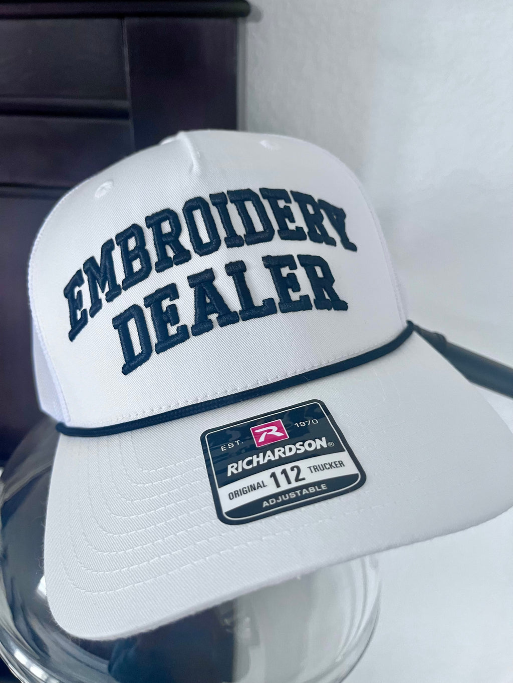 White cap with 'Embroidery Dealer' text and Richardson logo on a reflective surface.