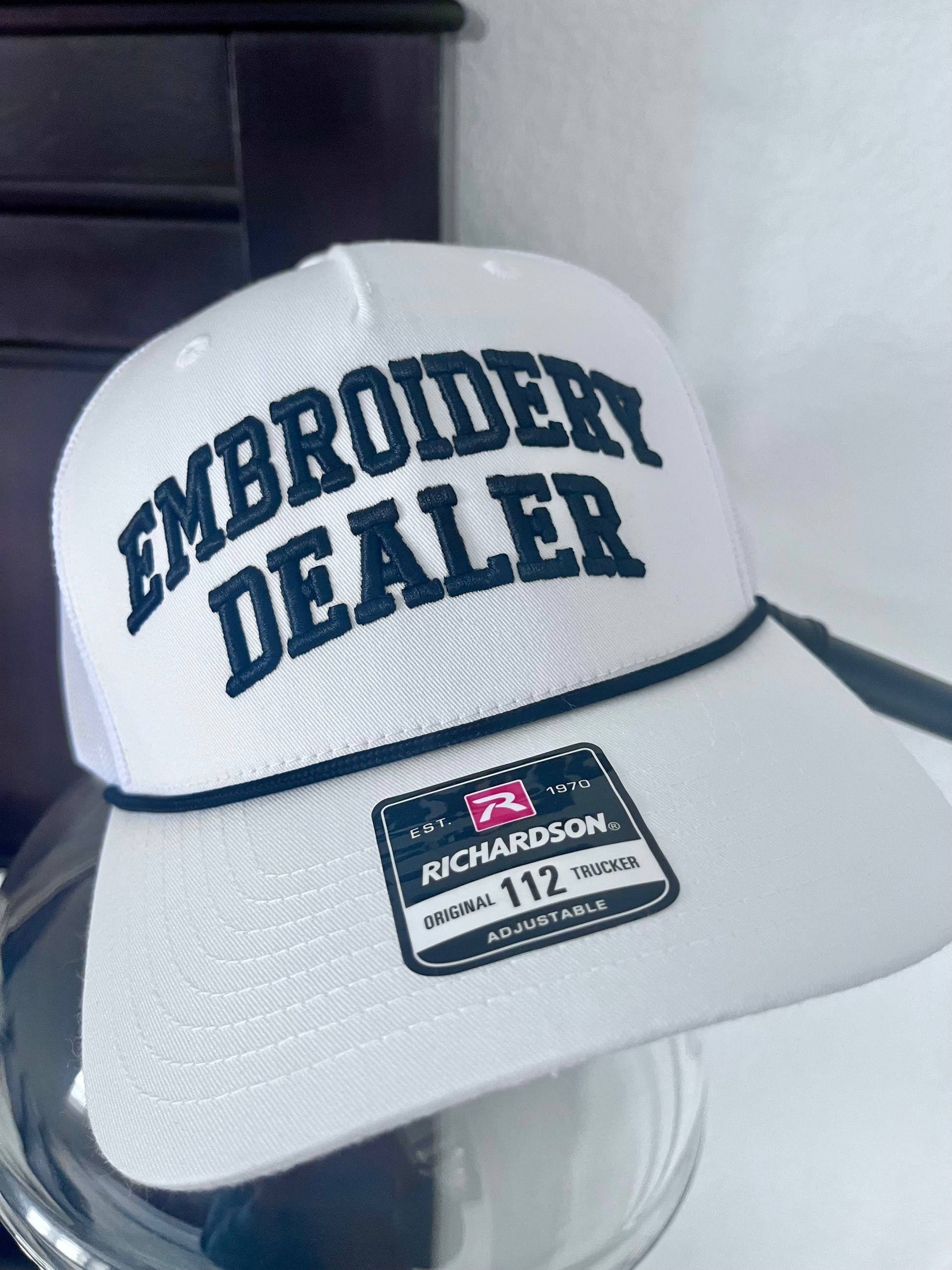 White cap with 'Embroidery Dealer' text and Richardson logo on a reflective surface.