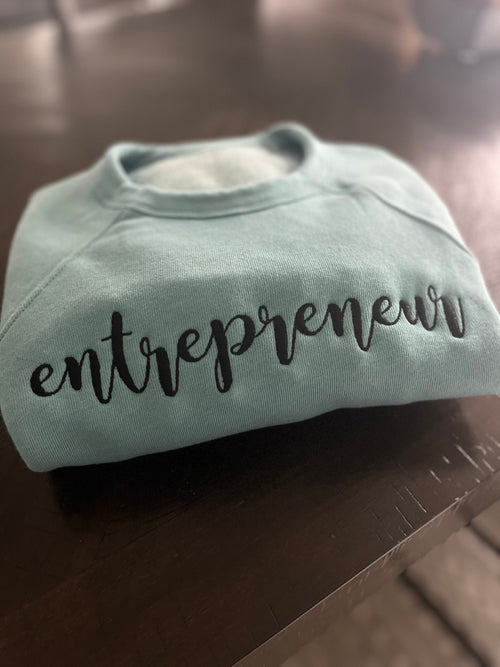 A blue embroidered crewneck sweatshirt with the word 'entrepreneur' written across the front in black thread.