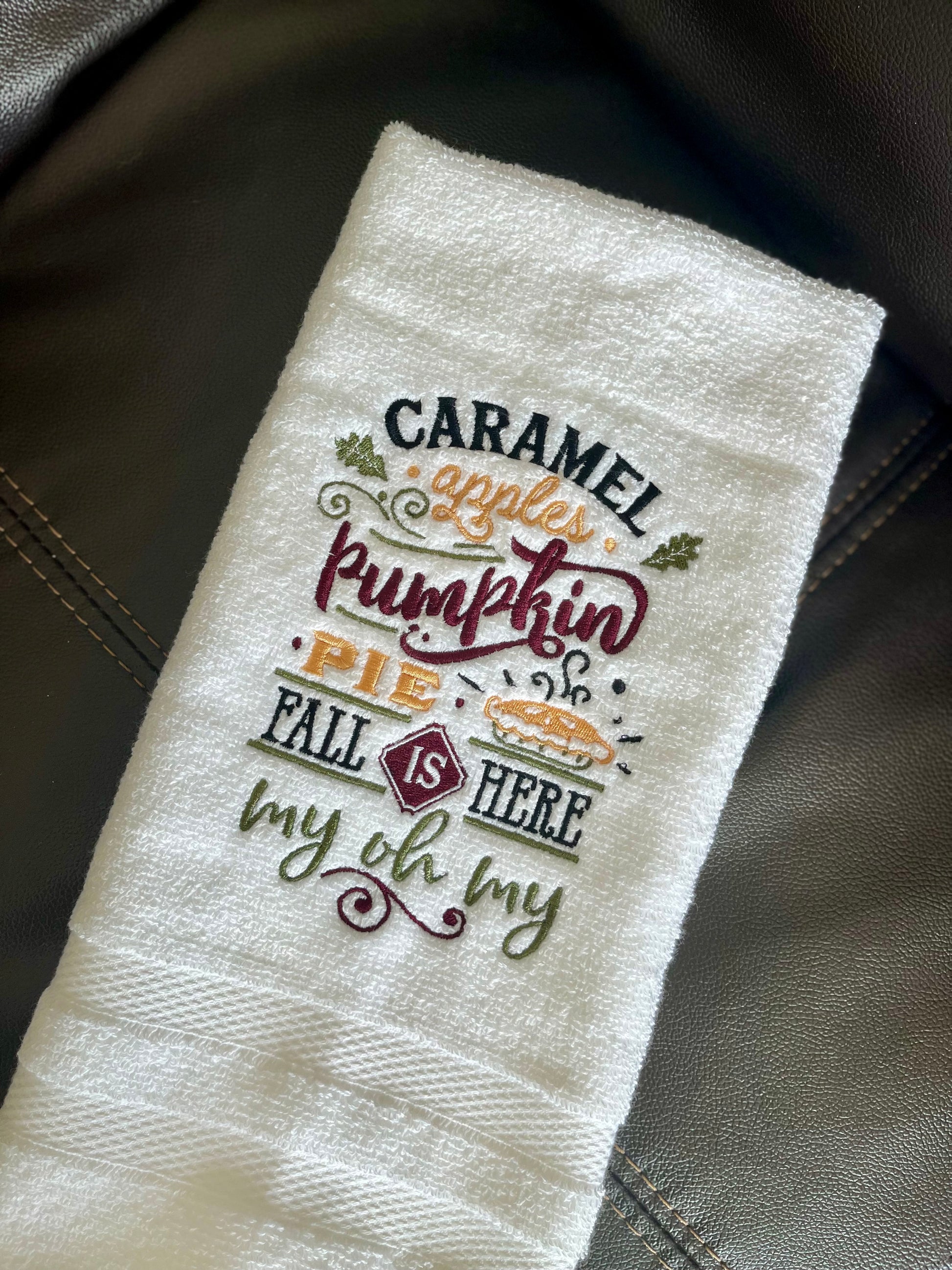 Embroidered towel with fall-themed text and graphics on a leather surface