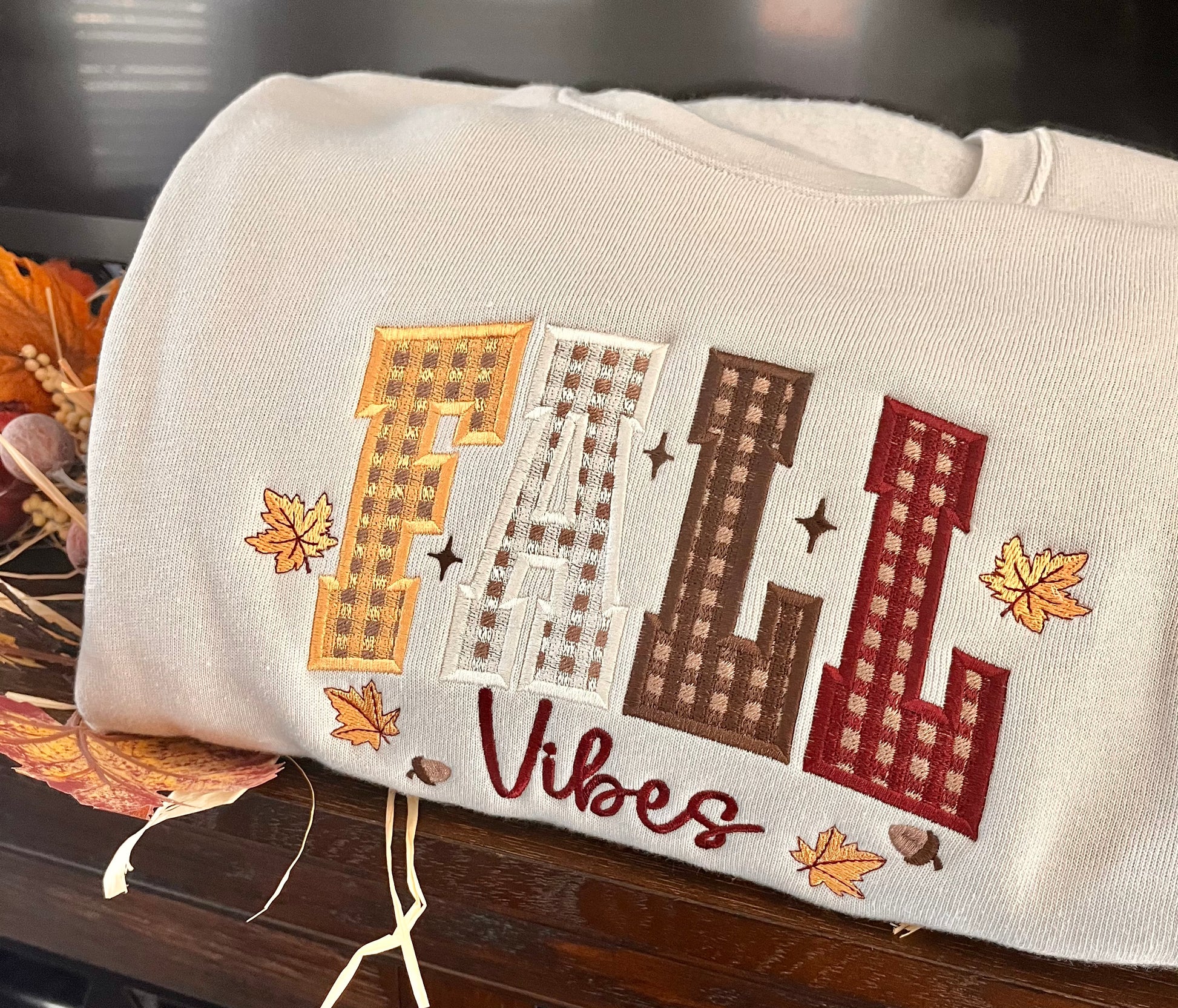 Beige pillow with embroidered 'Fall Vibes' text and fall-themed design on a wooden surface.