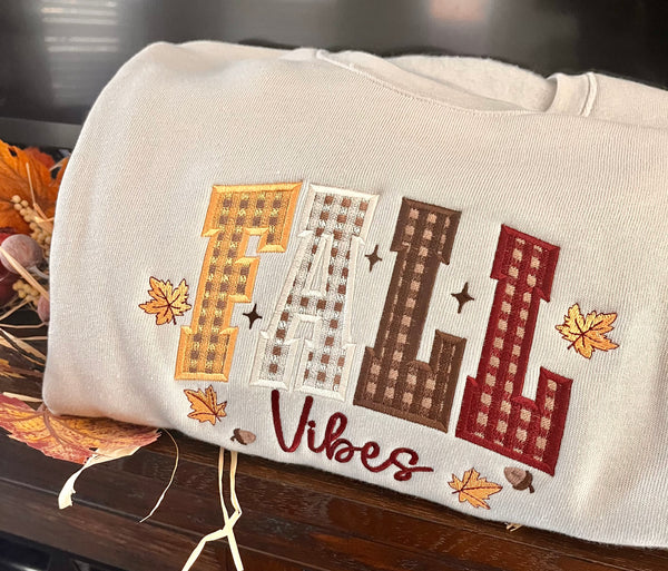 Beige pillow with embroidered 'Fall Vibes' text and fall-themed design on a wooden surface.