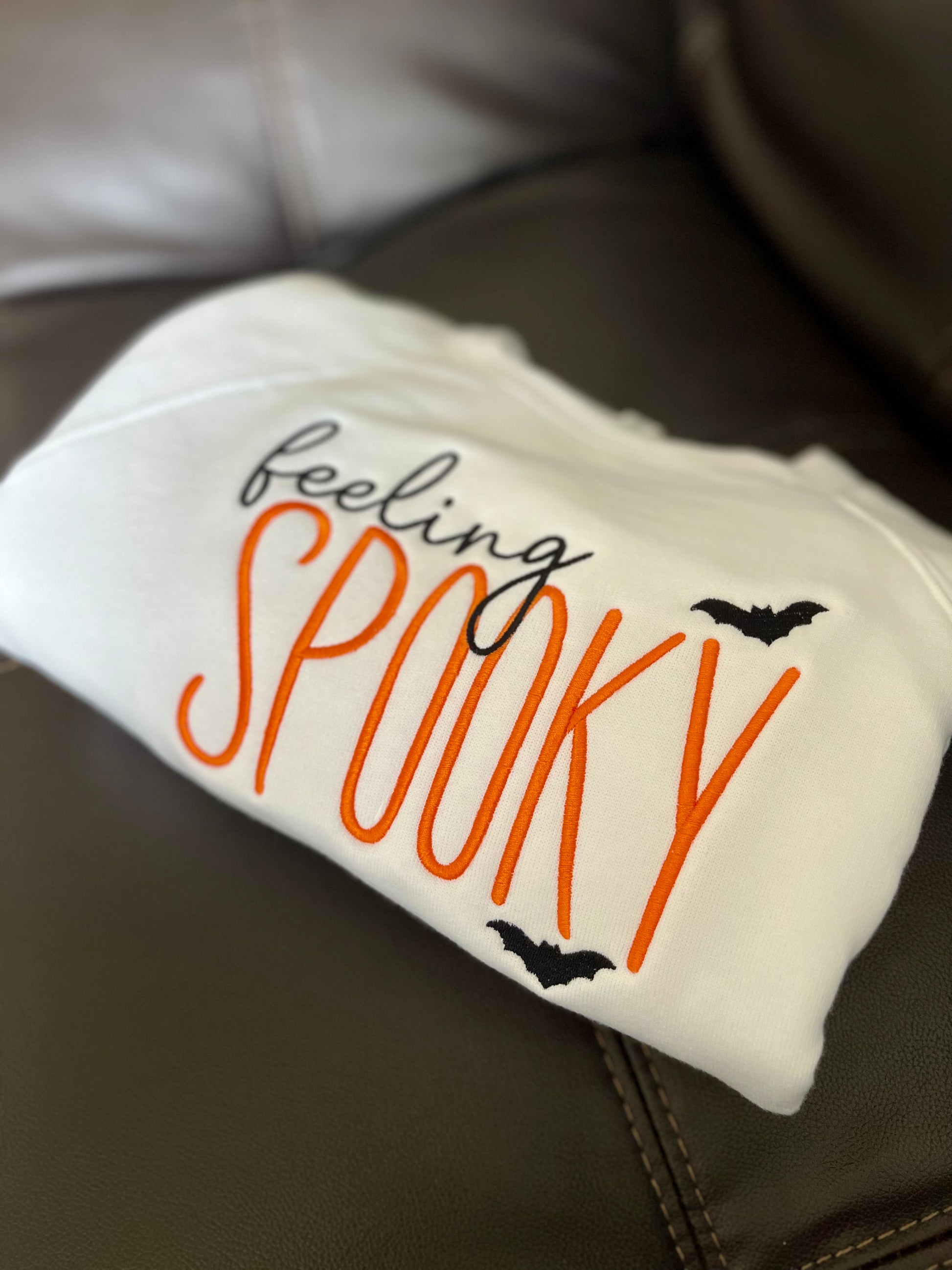 Folded white blanket with 'feeling spooky' text and bats on a brown surface