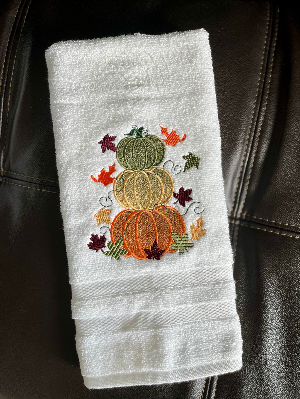White towel with embroidered pumpkins and leaves on a black leather surface