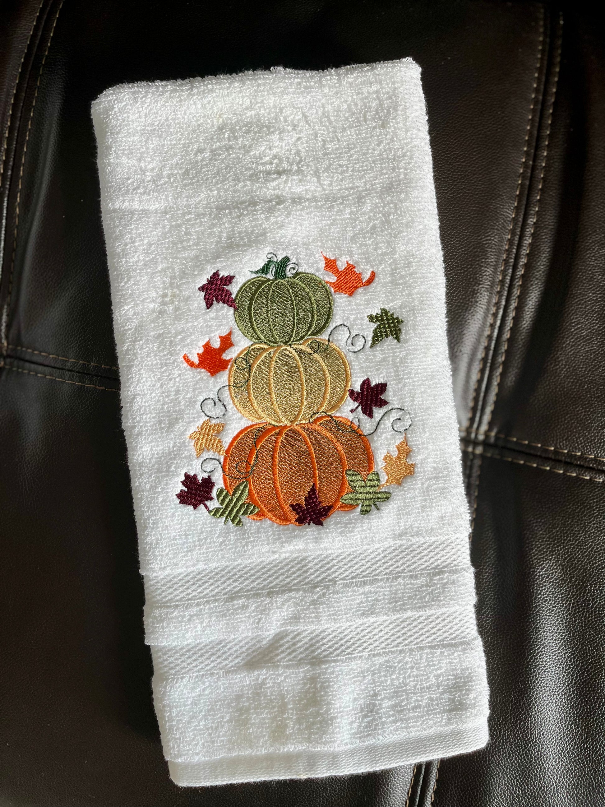 White towel with embroidered pumpkins and leaves on a black leather surface