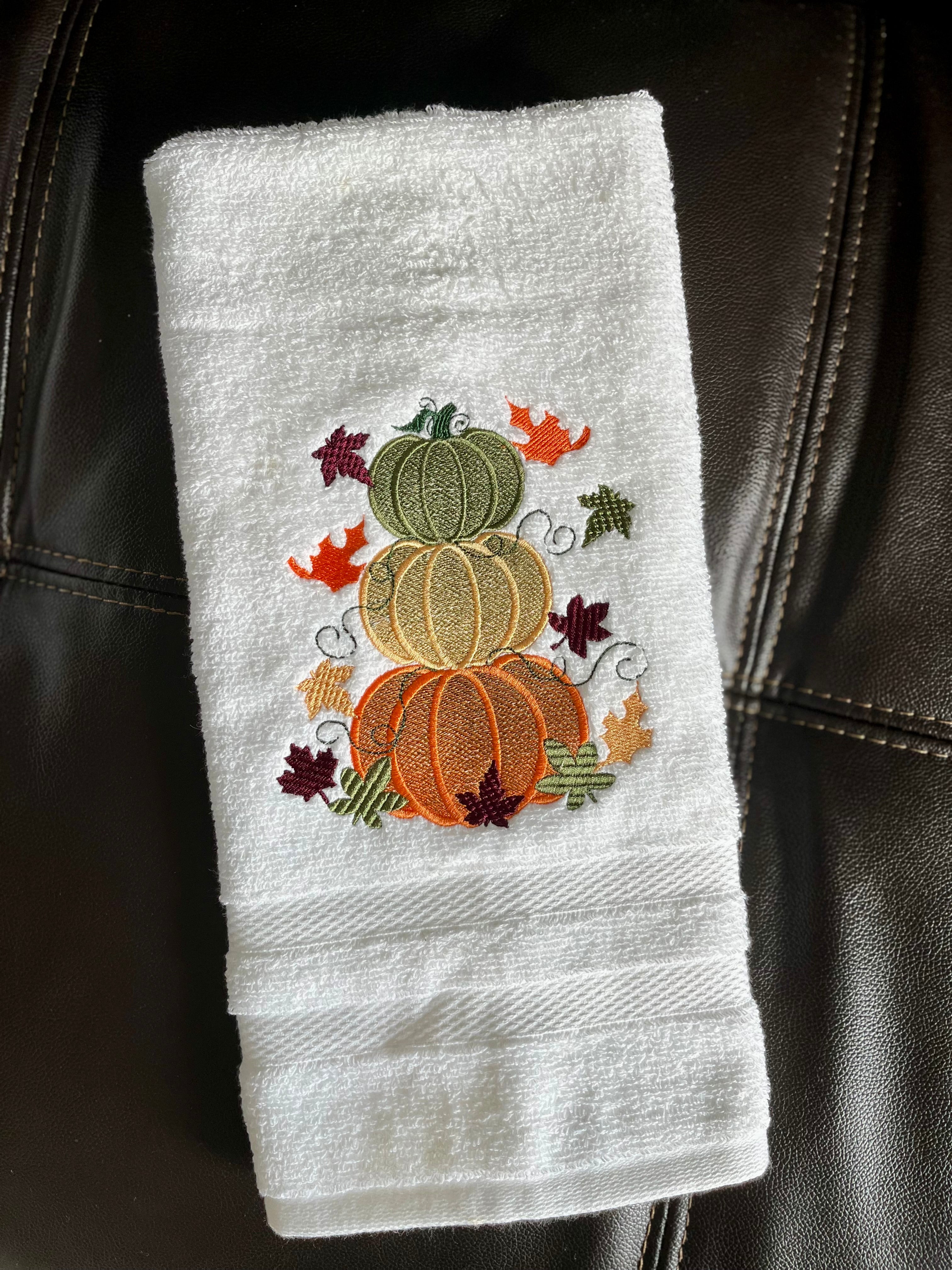 White towel with embroidered pumpkins and leaves on a black leather surface