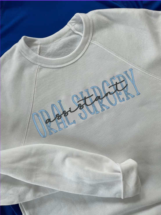 White crewneck sweatshirt with the text 'oral surgery assistant' embroidered on the front.