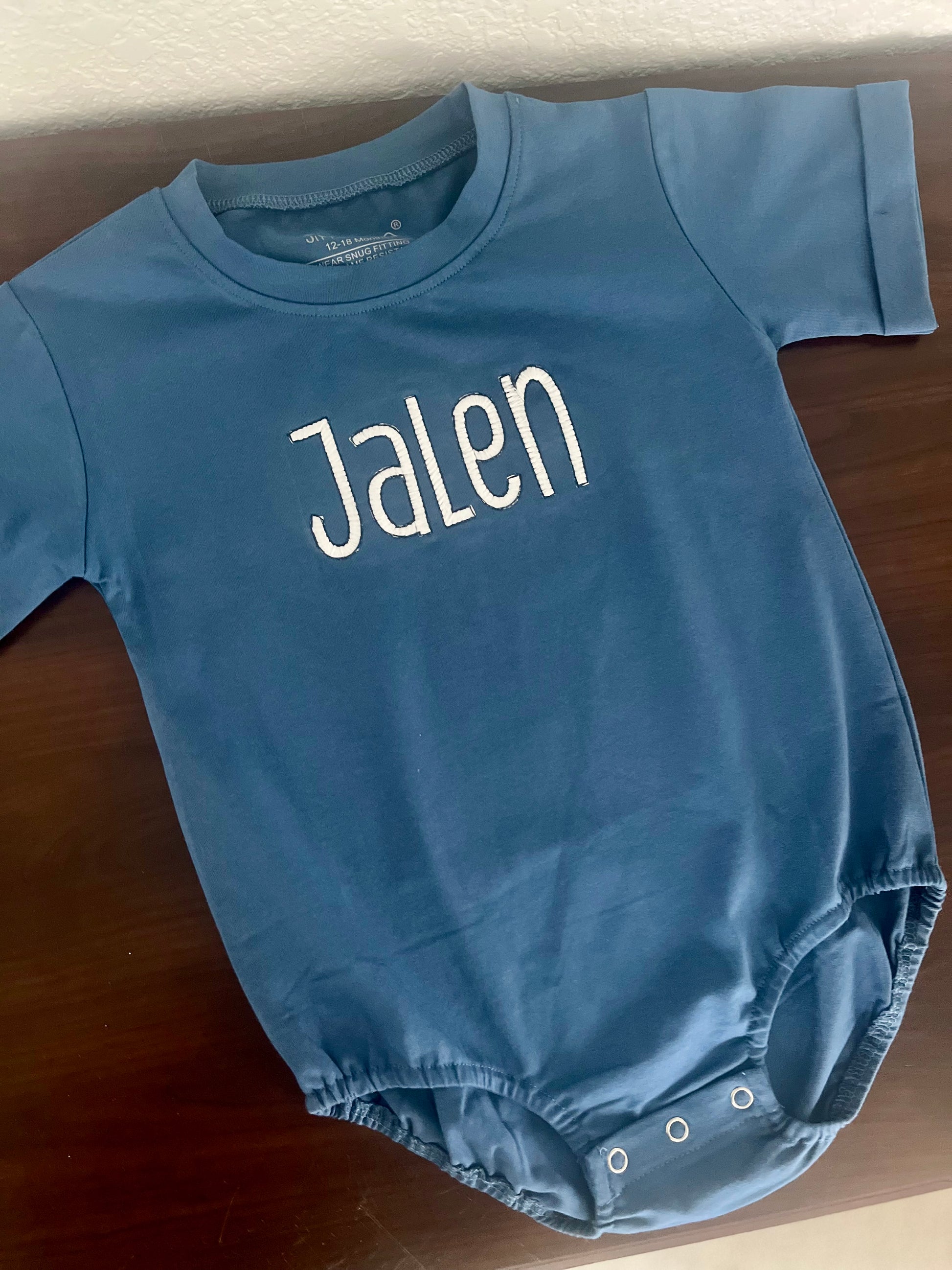 Personalized baby t-shirt romper , lying flat on a wooden surface.