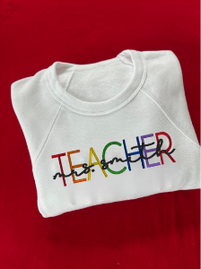 A white crewneck sweatshirt with the word 'TEACHER' embroidered in multicolored letters, on a red background.