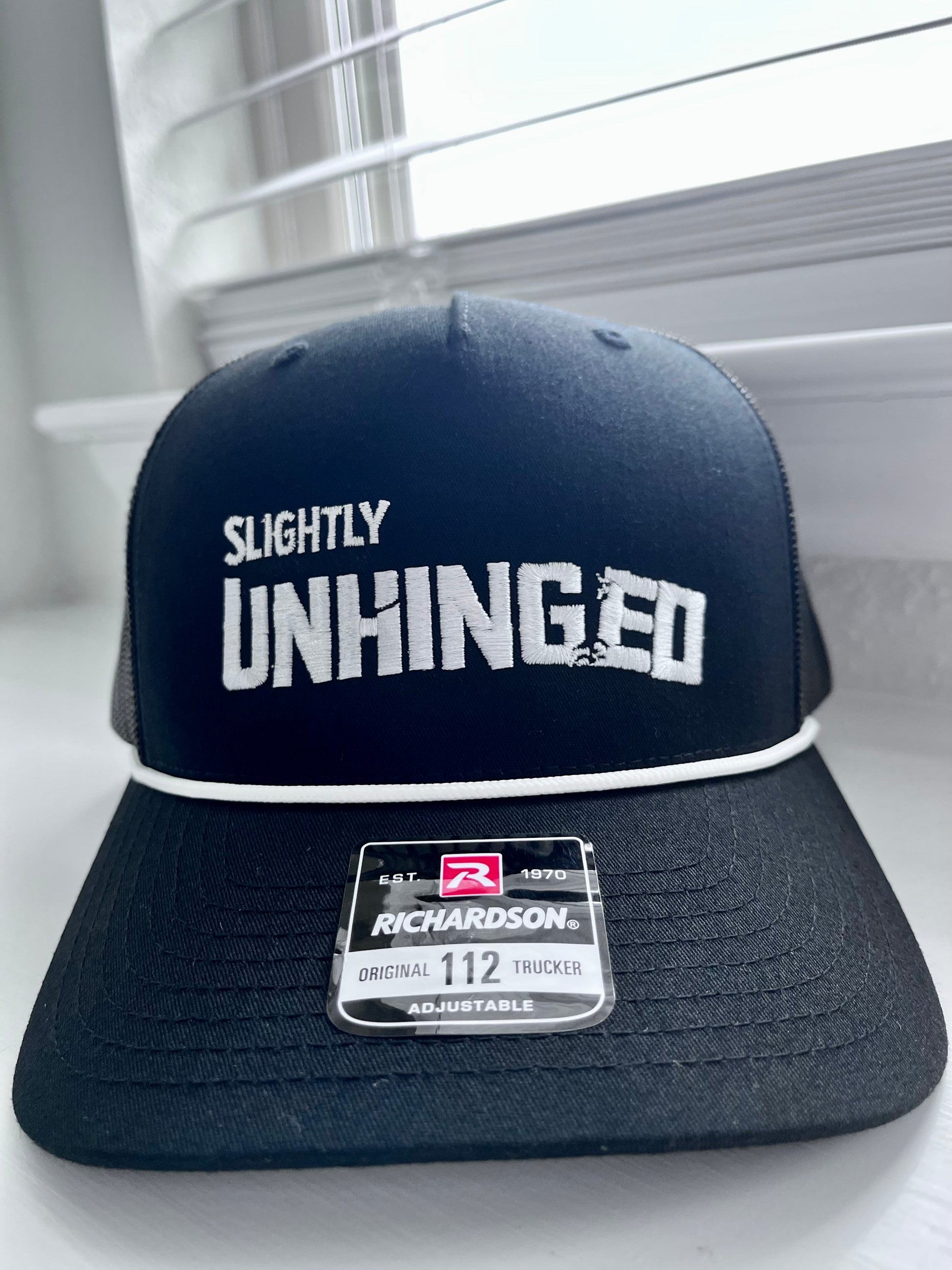 Navy blue cap with 'Slightly Unhinged' text on a white surface