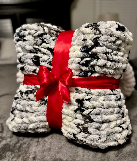 A chunky handknit blanket with black and white yarn, tied with a red ribbon.