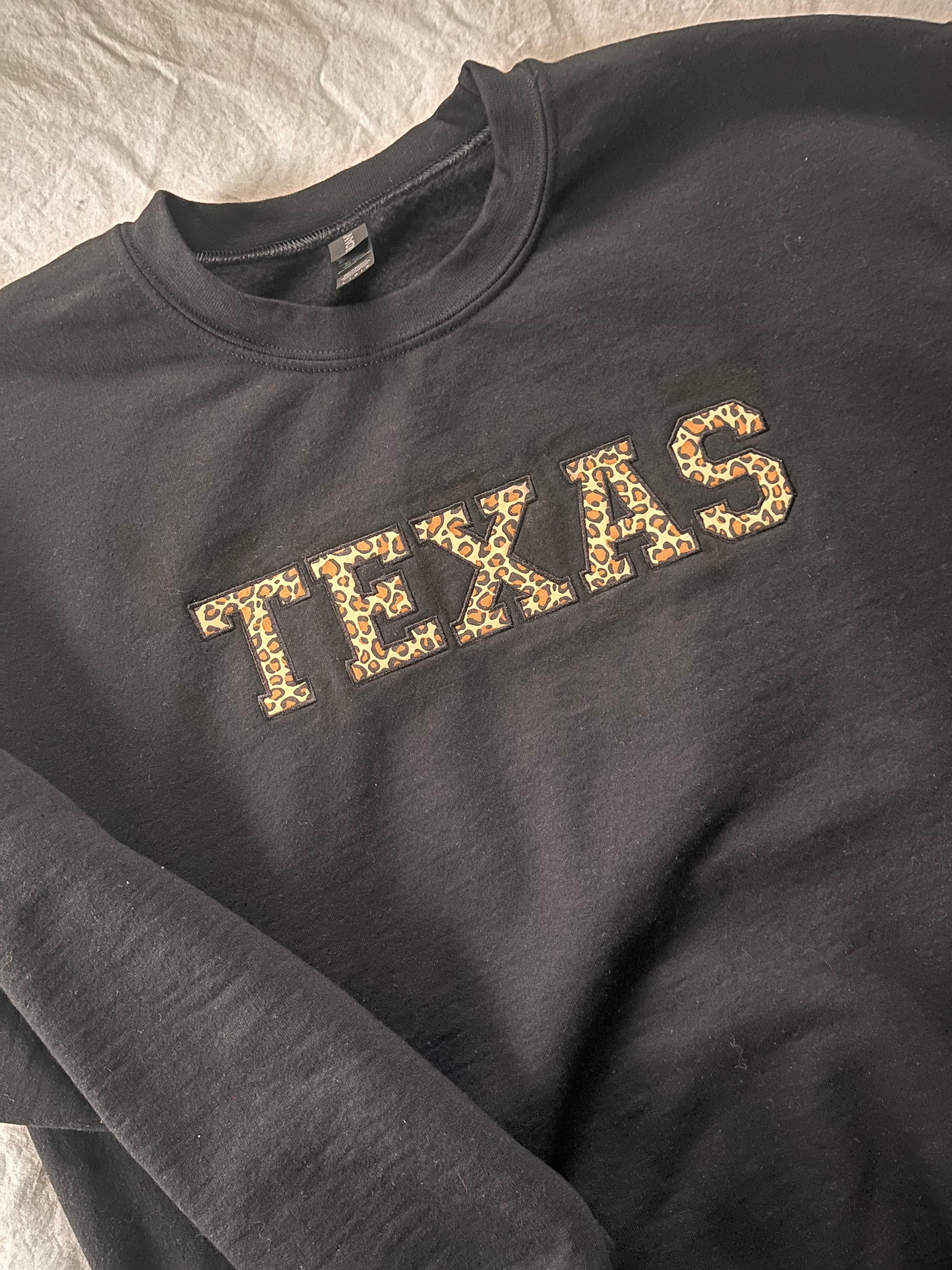 A gray crewneck sweatshirt with 'TEXAS' written across the front in a leopard print pattern.