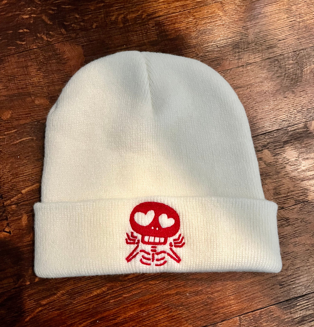 White beanie with a red skull design on a wooden surface