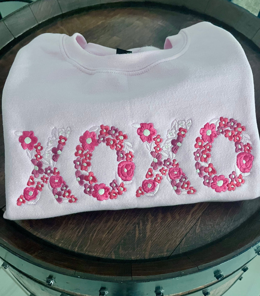 White sweatshirt with pink floral 'XOXO' design on a wooden surface